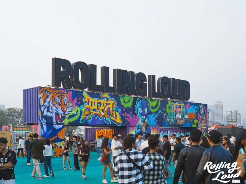 Crowd walking past the Doodle Mapuls mural wall under the Rolling Loud sign