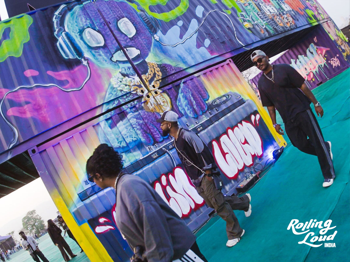 Artists painting a giant purple and neon mural on shipping containers